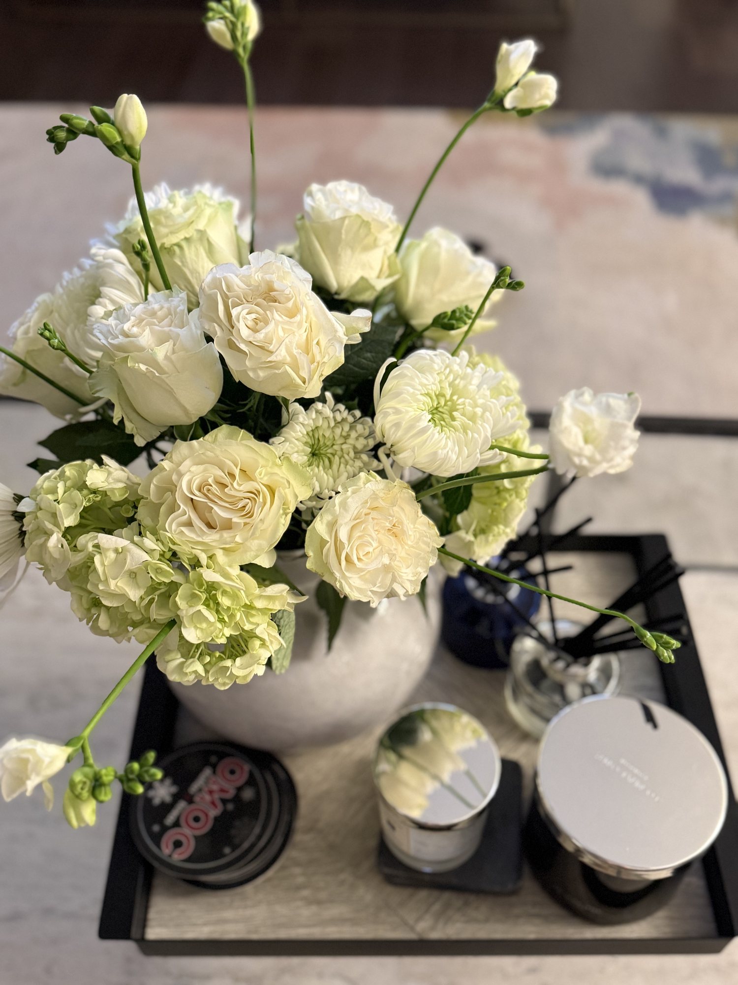 White roses, green hydrangea, and white lisianthus in a round white vase on a black tray
